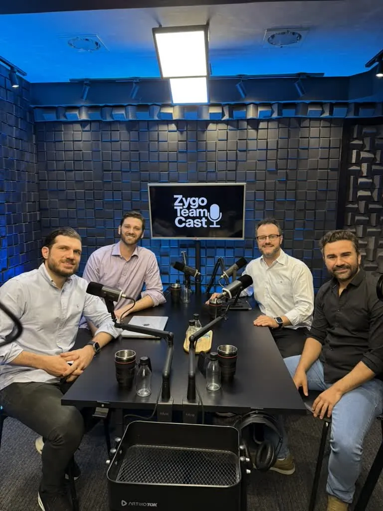 Quatro pessoas à mesa em um cenário azul do Zygo Team Cast