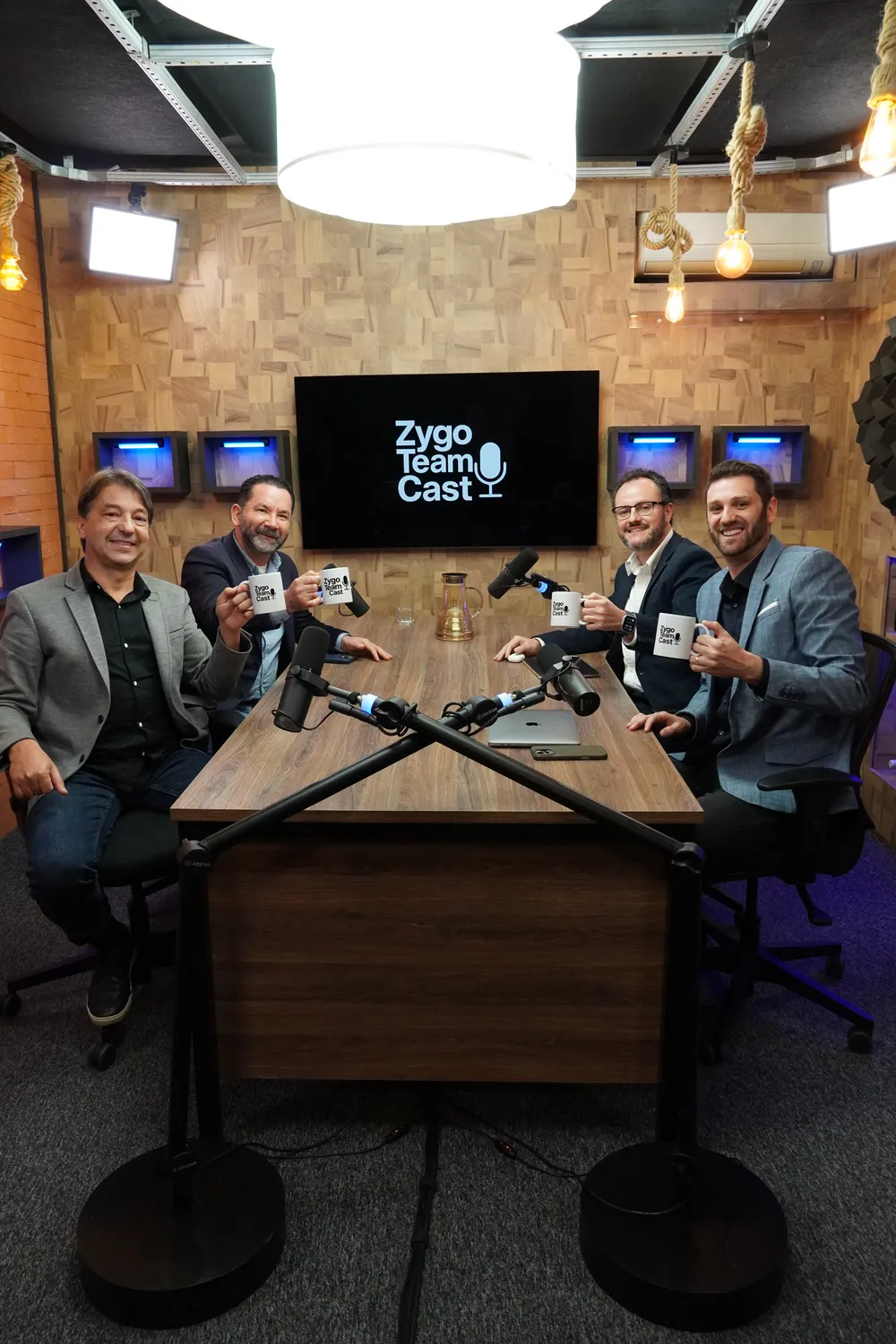 O estúdio do Zygo Team Cast, com os apresentadores à mesa segurando canecas do podcast